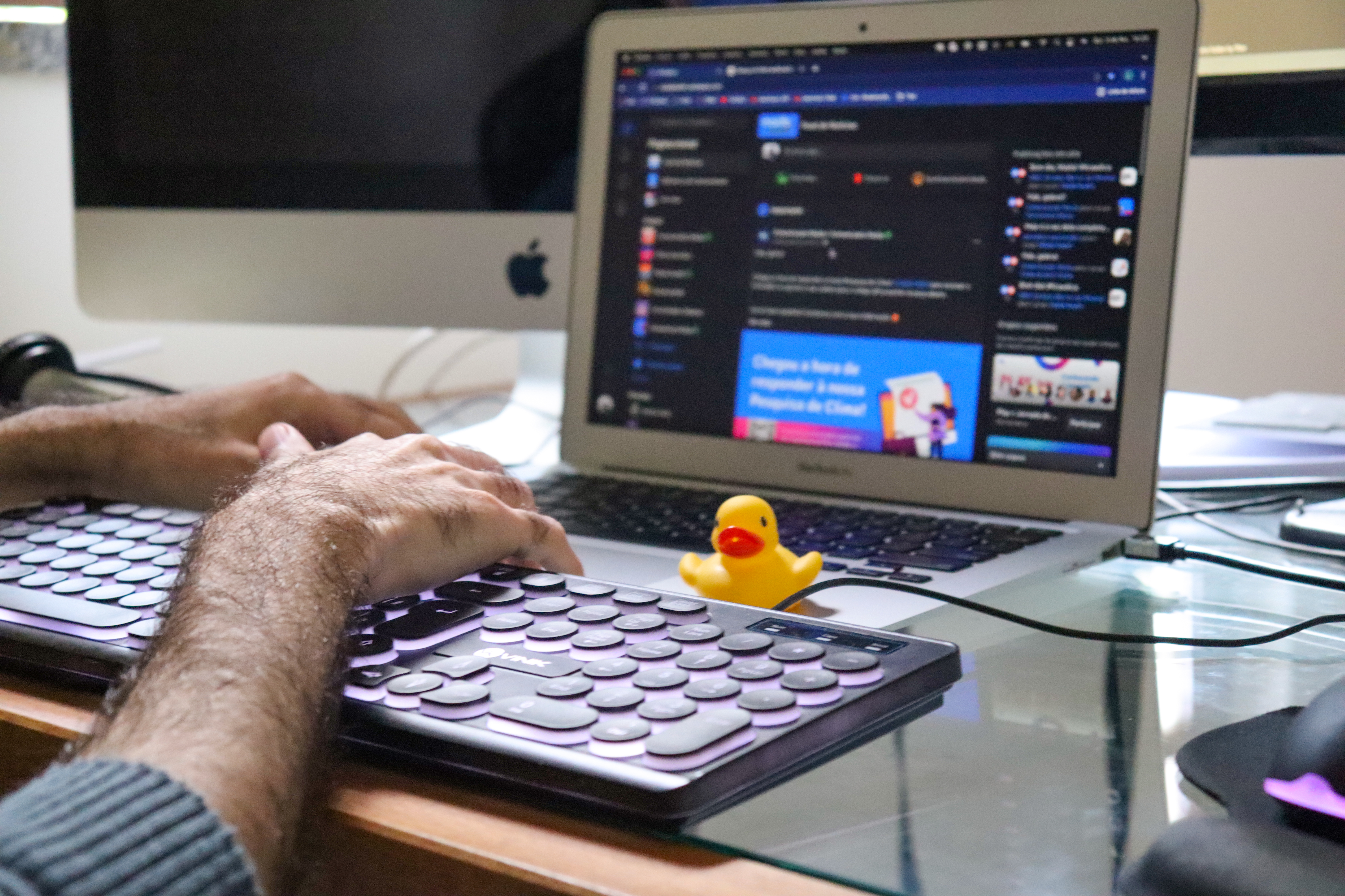 Estudante de engenharia de software do iCEV trabalhando no laptop com pato de borracha amarelo próximo ao teclado 